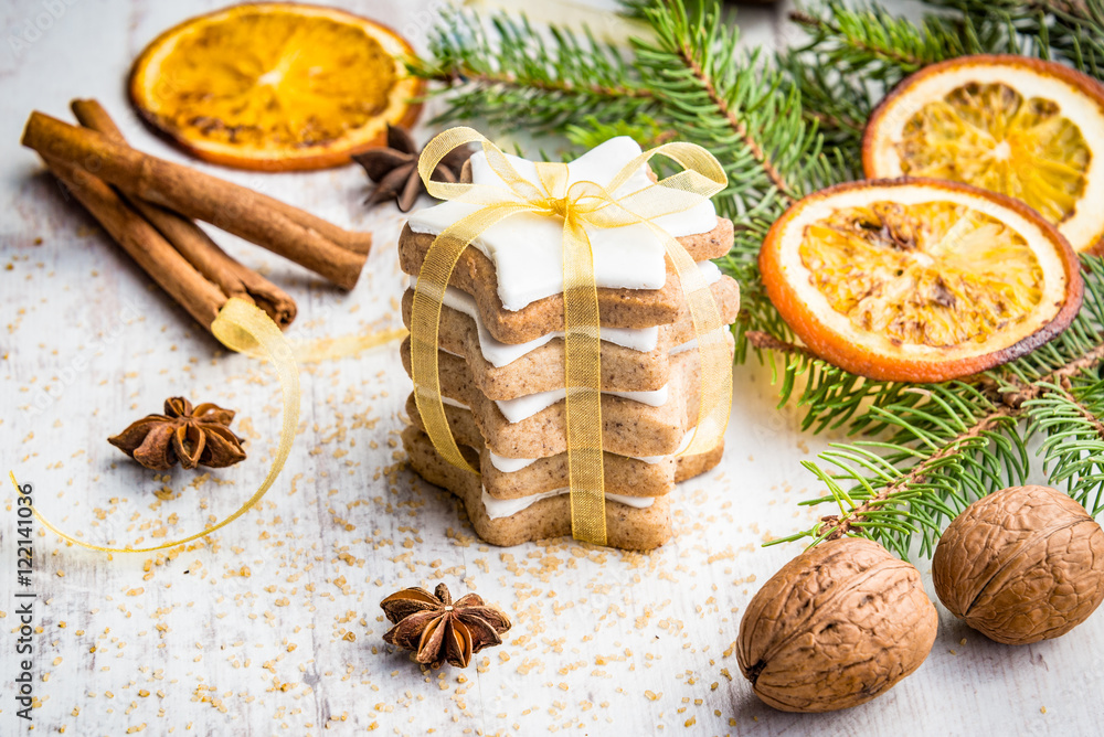 Close up of homemade butter nuts star shaped cookies with icing, pine, orange slices,cinnamon, anise, walnuts and golden ribbon over white wood background. Christmas decoration.