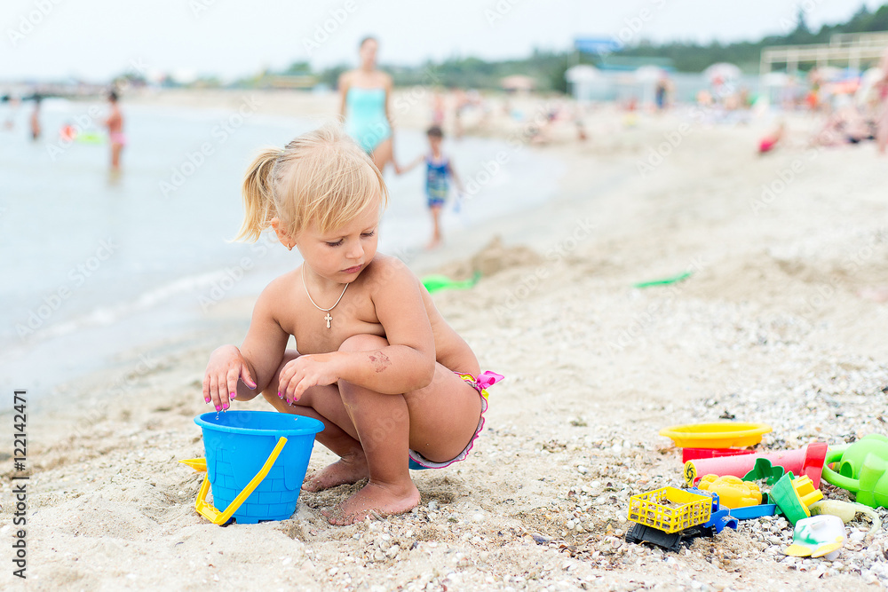 Adorable toddler girl playing with beach toys on white sand beach Adorable toddler girl playing with beach toys on white sand beach