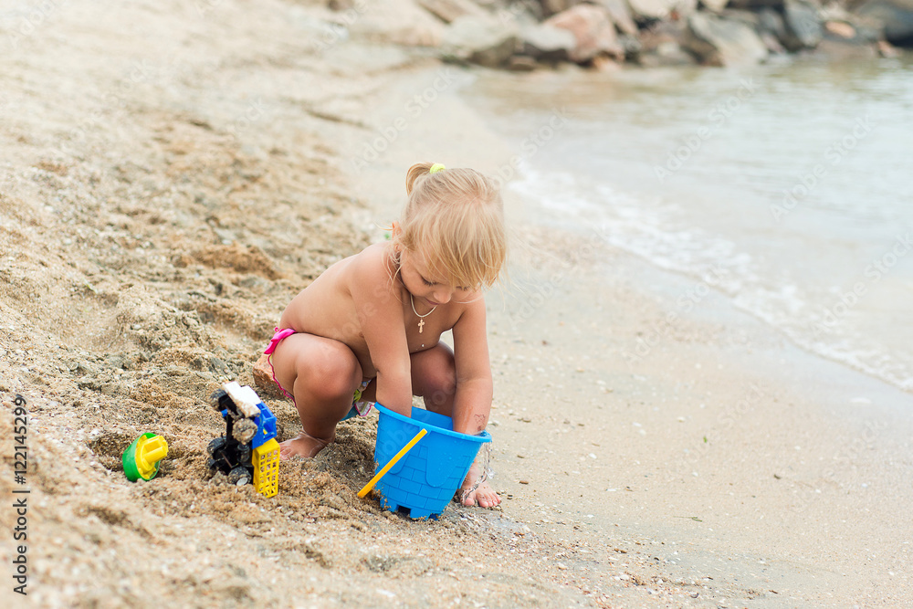 Adorable toddler girl playing with beach toys on white sand beach Adorable toddler girl playing with beach toys on white sand beach