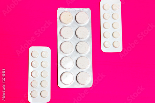Three packs of pills lying on the pink background.