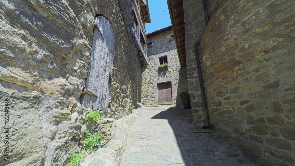 RUPIT CATALONIA SPAIN - JULY 2016: Smooth camera steady wide angle shot along narrow street in the old european spain village goes up, high colorful ancient walls with windows, clear sky with sun