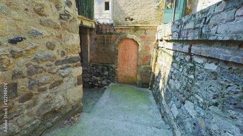 BESALU CATALONIA SPAIN - JULY 2016: Smooth camera steady wide agle shot along narrow street in the old european spain village goes up, high colorful ancient walls with windows, clear blue sky with sun photo