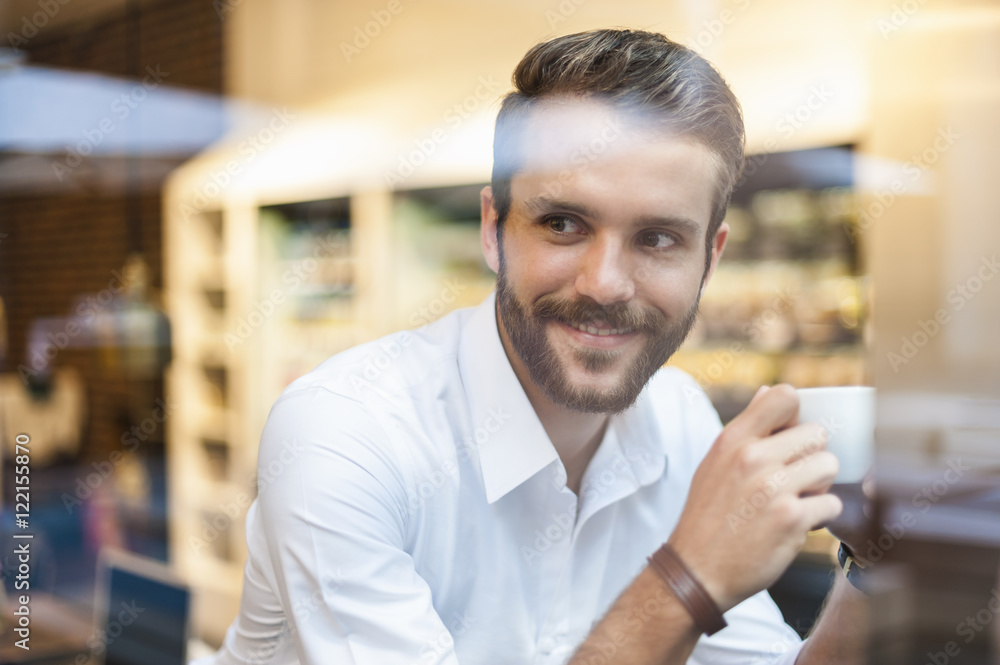 Smiling businessman holding cup of coffee behind windowpane in a cafe Smiling businessman holding cup of coffee behind windowpane in a cafe