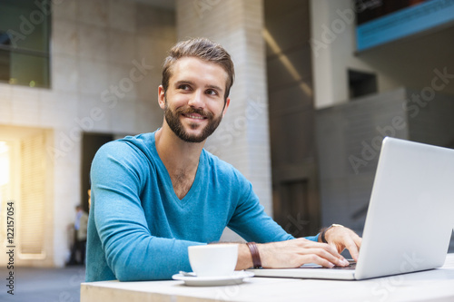 Smiling young man sitting at table using laptop