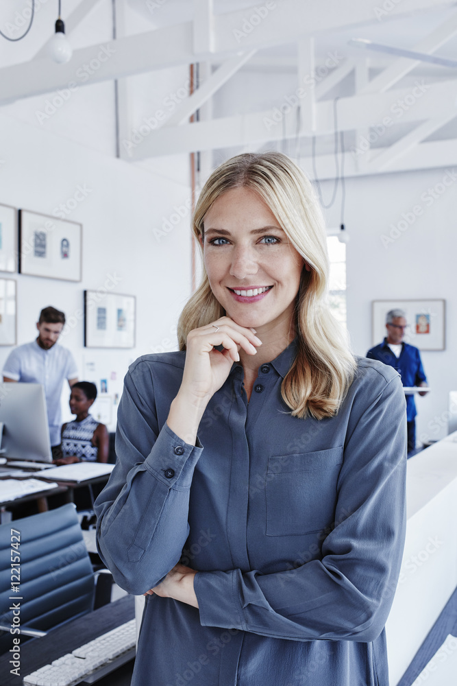 Portrait of smiling businesswoman in office with staff in background Portrait of smiling businesswoman in office with staff in background