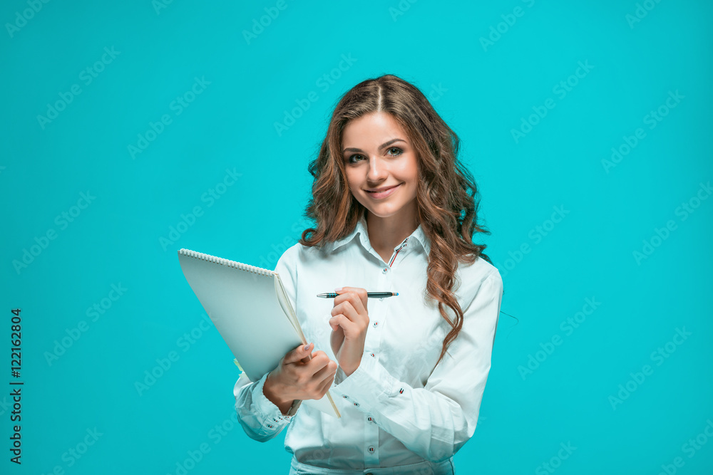 The smiling young business woman with pen and tablet for notes on blue background The smiling young business woman with pen and tablet for notes on blue background