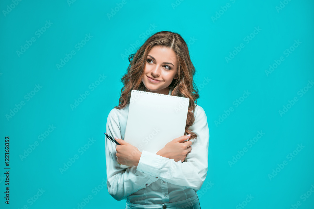 The smiling young business woman with pen and tablet for notes on blue background The smiling young business woman with pen and tablet for notes on blue background