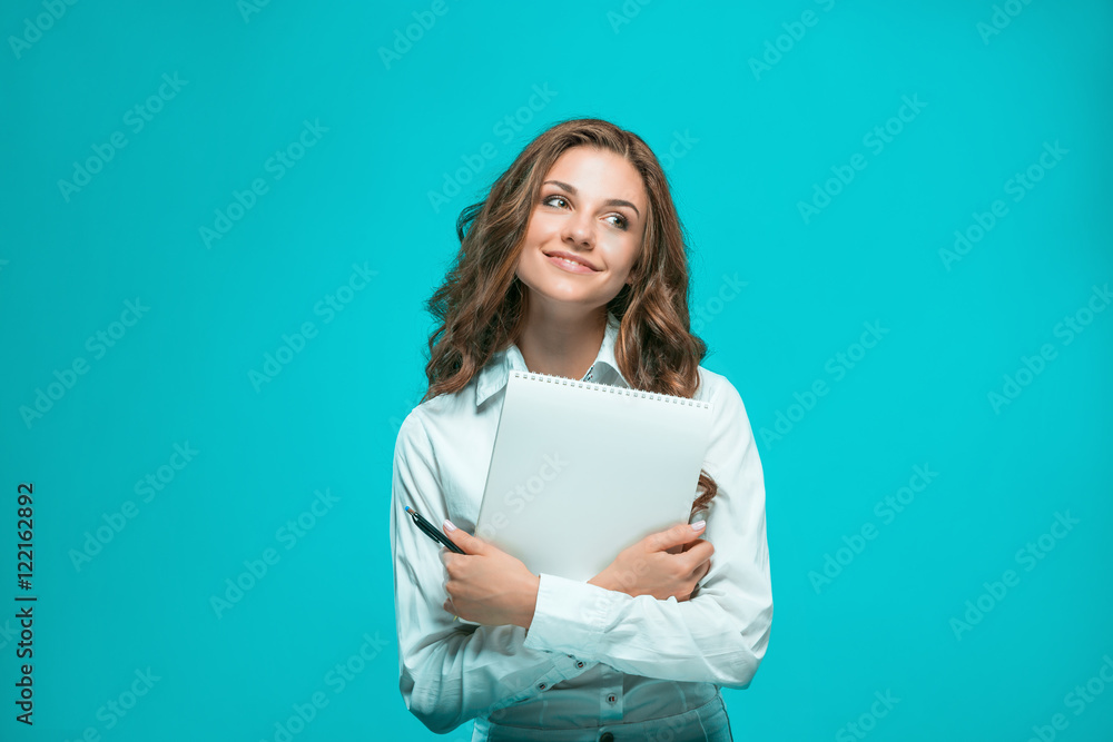The smiling young business woman with pen and tablet for notes on blue background The smiling young business woman with pen and tablet for notes on blue background