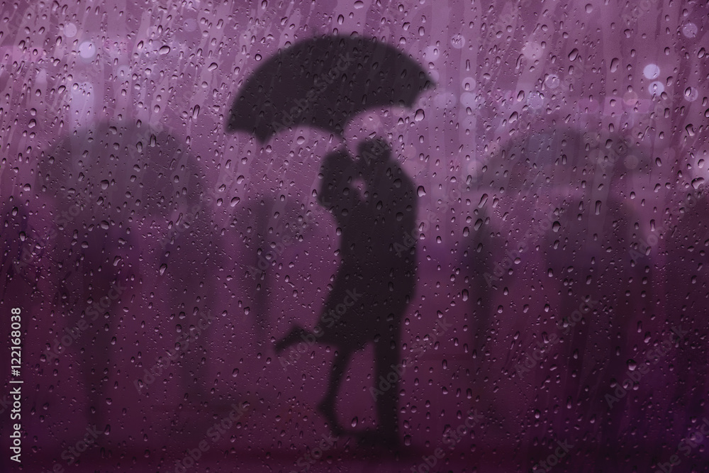 Blurred lover Kissing in the Rain among people with Umbrella on the Street at night, See through Glass Window, Selective focus on droplet