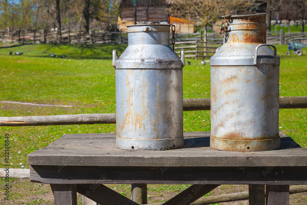 Metal milk churns stand on wooden table