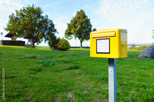 Yellow German postbox one in the green meadow in village