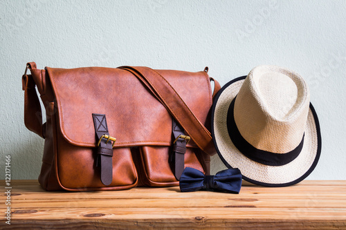 Fototapeta Naklejka Na Ścianę i Meble -  Men's accessories with brown leather bag, brown hat and blue bow tie on wooden table over wall background