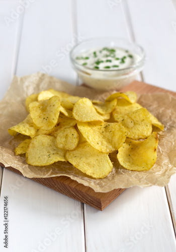 Potato chips on a parchment with a dipping sauce on a white table.