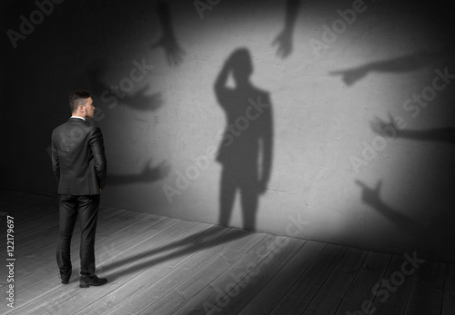 Tableau sur toile Businessman looking at shadow where many hands reach for him forcing grab his head