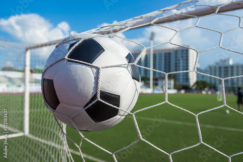 soccer ball in goal net with green grass blue sky