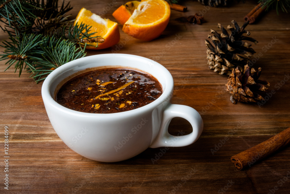 Hot chocolate with spices, orange and orange zest. Against the background of Christmas tree branches, cones and orange. Wooden table Hot chocolate with spices, orange and orange zest. Against the background of Christmas tree branches, cones and orange. Wooden table