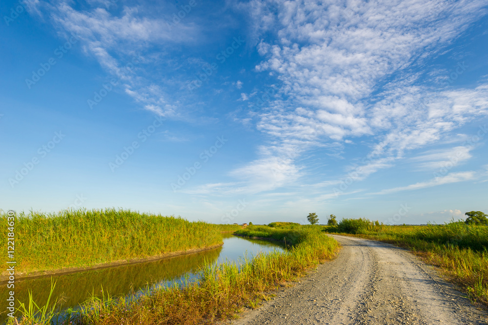 Curvy gravel road and irrigation canal with nice cloudy blue sky Curvy gravel road and irrigation canal with nice cloudy blue sky
