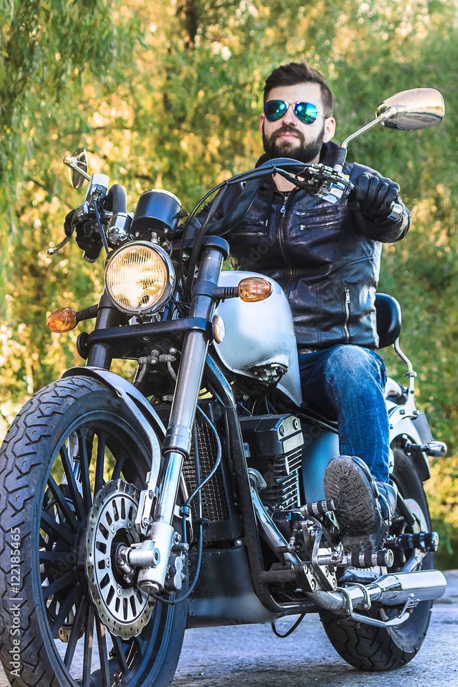 Biker man wearing a leather jacket and sunglasses sitting on his motorcycle Biker man wearing a leather jacket and sunglasses sitting on his motorcycle