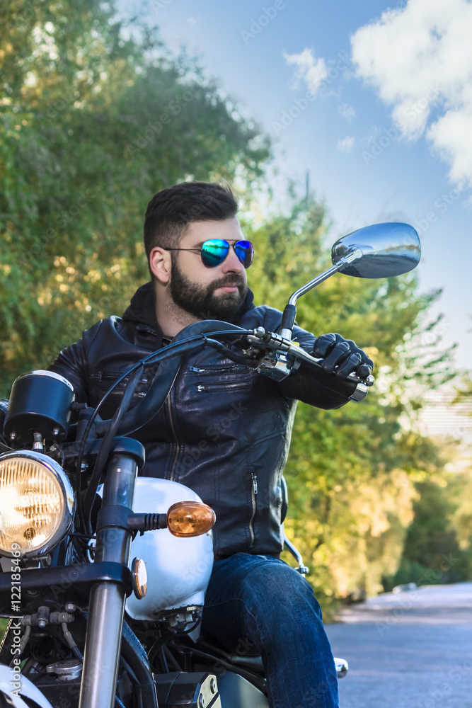 Biker man wearing a leather jacket and sunglasses sitting on his motorcycle