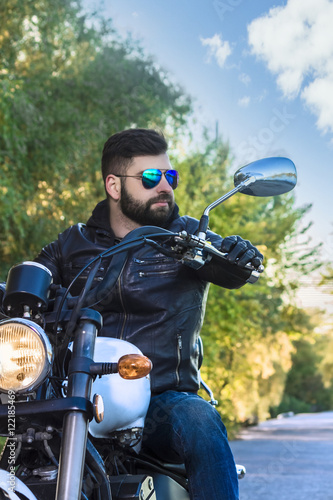 Biker man wearing a leather jacket and sunglasses sitting on his motorcycle