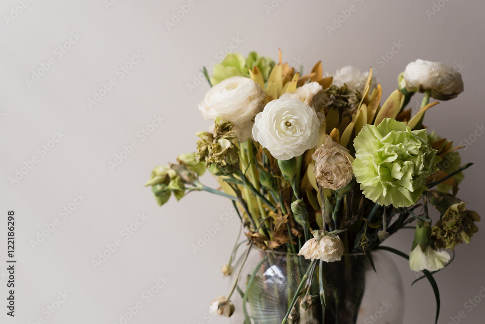 Close up of wilting green and white ranunculus and carnations in glass vase (selective focus)