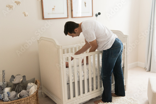 HIspanic dad putting newborn baby in crib photo