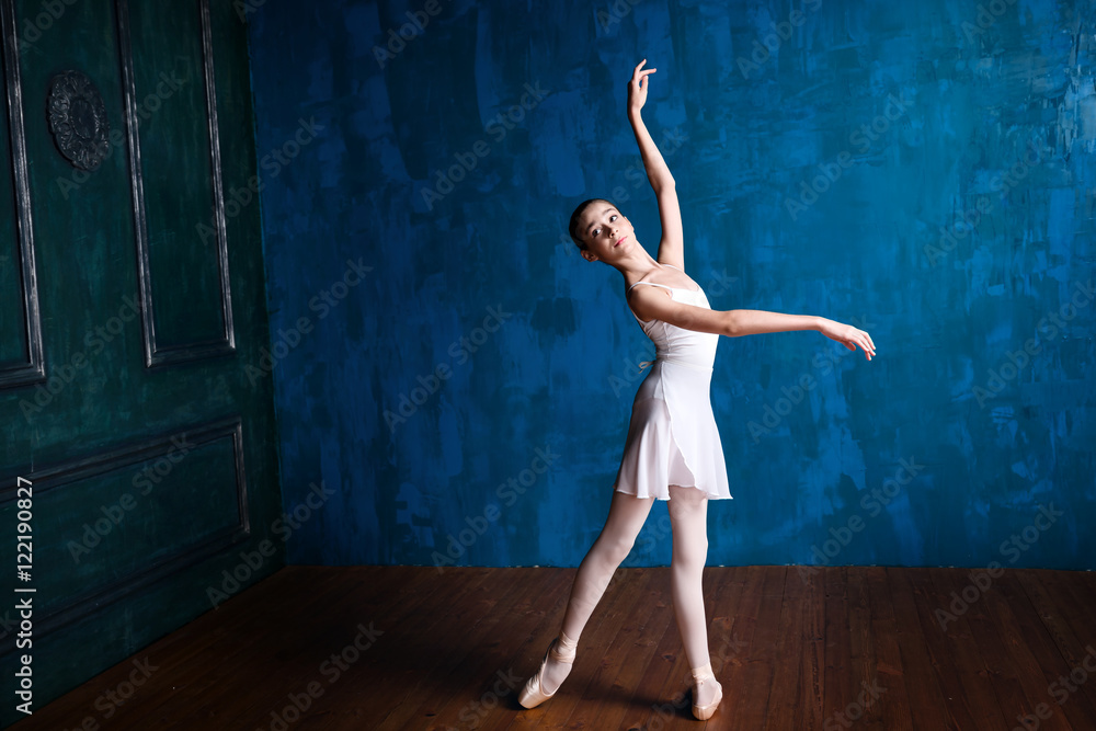 Fototapeta premium Young teenage ballerina is dancing and posing in the photostudio with blue walls