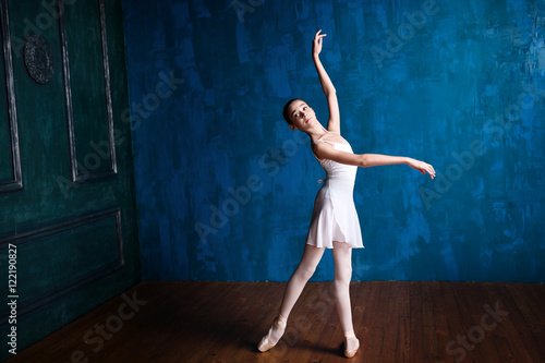 Young teenage ballerina is dancing and posing in the photostudio with blue walls