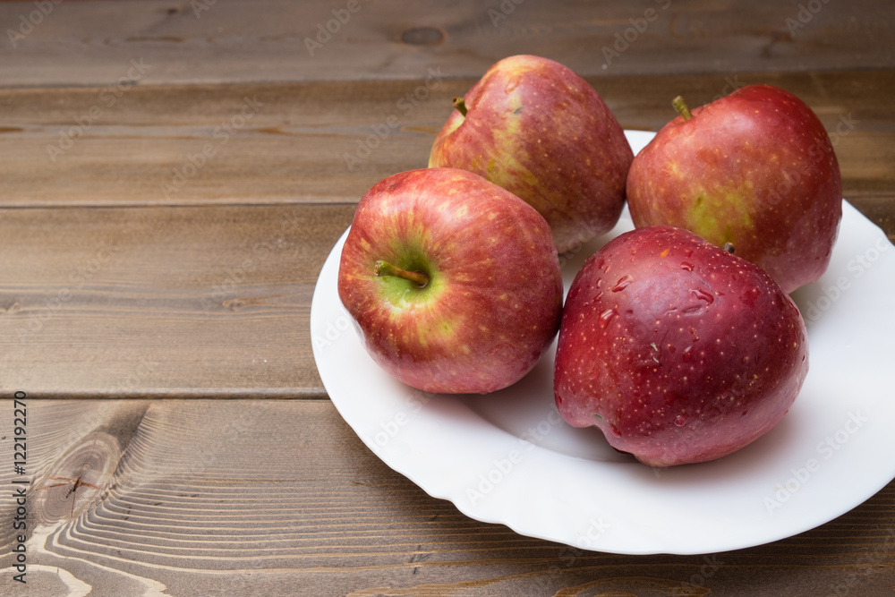 Four fresh red apples in white plate on wooden background Four fresh red apples in white plate on wooden background