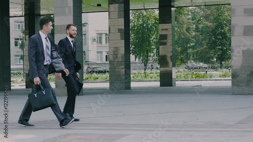 Two confident young businessmen are walking in the urban environment to the office building