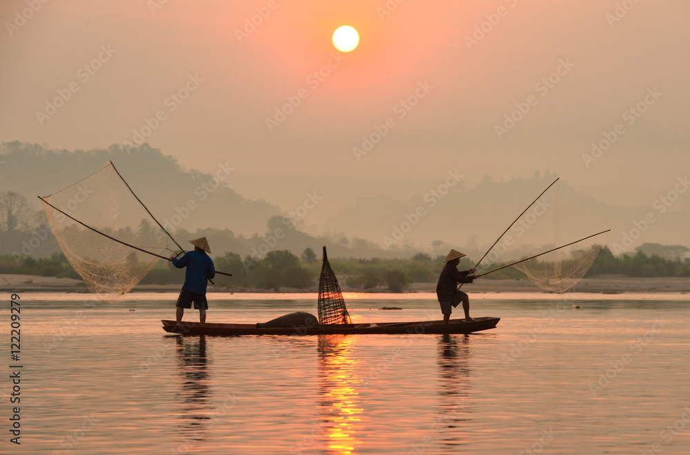 The silluate fisherman casting a net into the water on during sunrise,Thailand