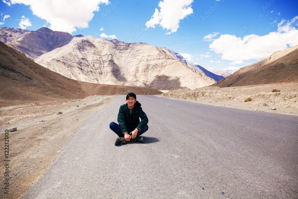 Young Asian male traveler sitting in the middle of empty road with freedom and joy in Leh, Ladakh, India