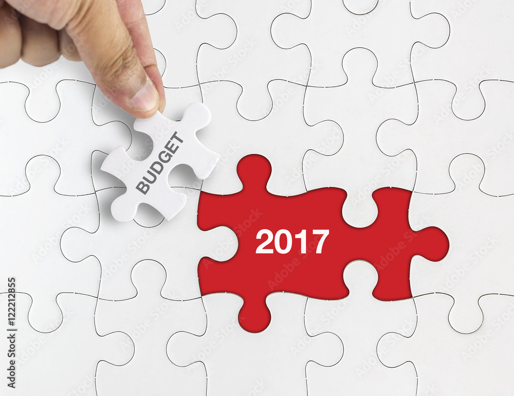 Fototapeta premium Hand holding piece of jigsaw puzzle with word BUDGET 2017.