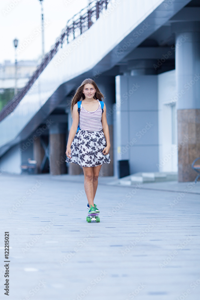 Young cute school girl rides skateboard on road
