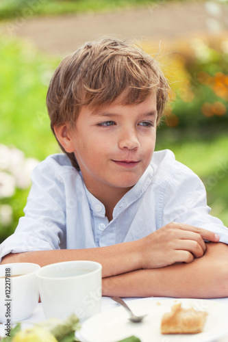 Happy nice boy drinking tea in summer green garden