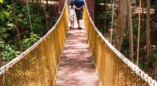 behind of unknown girl and man walking across nylon bridge at public park © ochong
