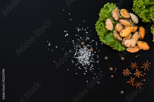 Preparing fresh seafood in the kitchen with gourmet mussels surrounded by fresh herbs and spices on black stone background