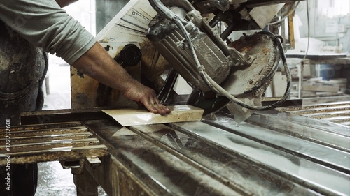 Worker uses saw machine for cutting marble stone piece , close up
