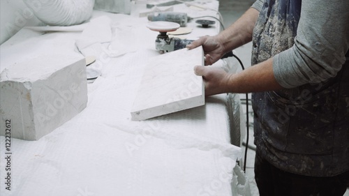 Worker polishes the piece of marble stone with tools photo