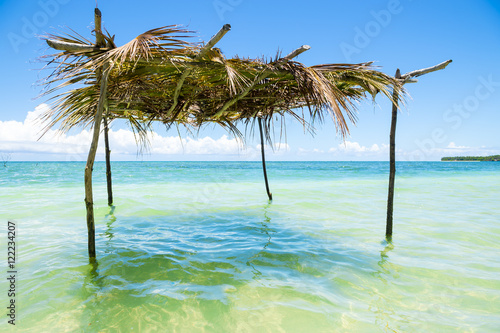 Rustic palm frond and tree branch palapa umbrella stands waiting to shade visitors to the shallow waters on a remote tropical beach in Nordeste northeastern Bahia  Brazil