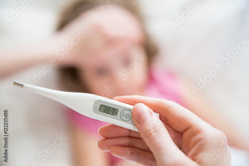 Close-up thermometer.  Mother measuring temperature of her ill kid. Sick child with high fever laying in bed and mother holding thermometer. Hand on forehead.  photo