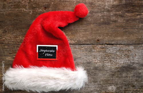 chapeau de Noël avec petit panneau "joyeuses fêtes" sur fond bois