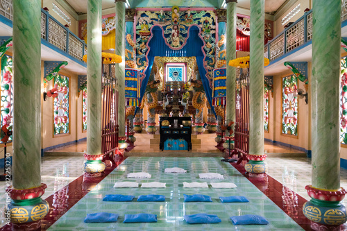 Interior of Buddhist temple with high columns and bright colorful walls. Pillows for pray are laying down on the floor before an Buddhist deity altar