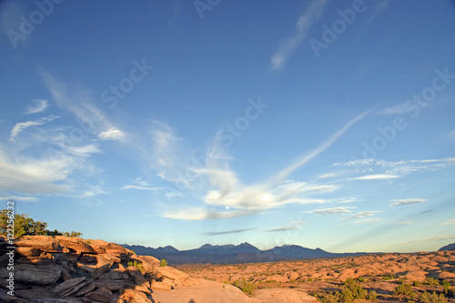 Desert sunset wide angle with mountains in background and clouds and brush and moon