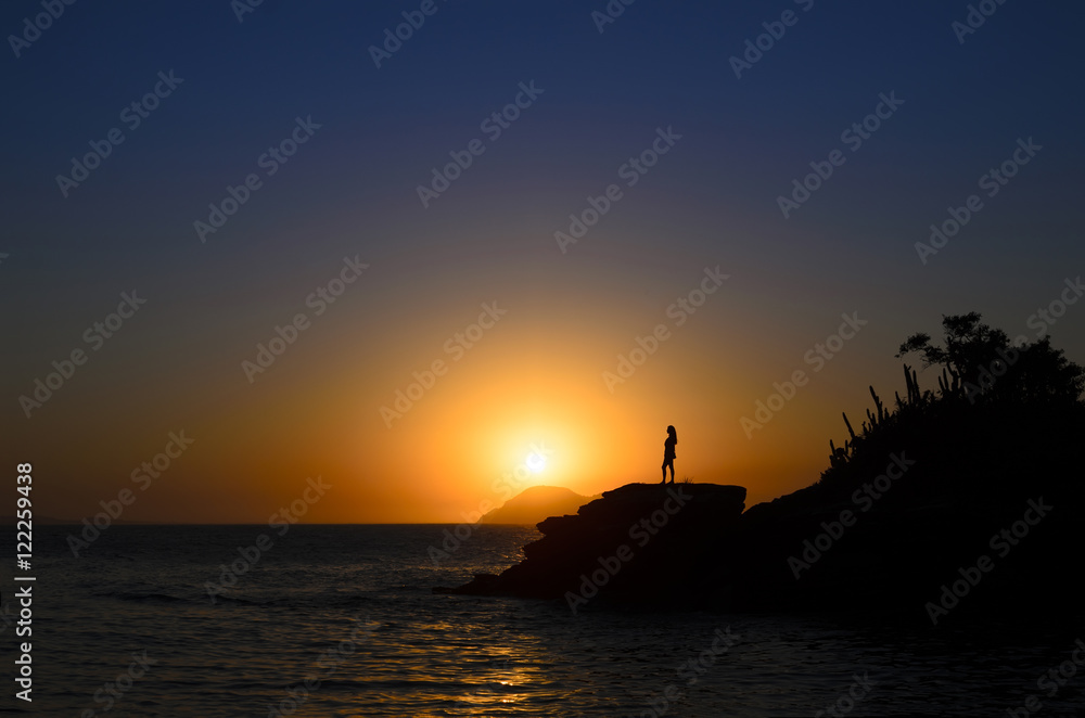 Silhouette of a woman standing at the breakage at the rosky beac