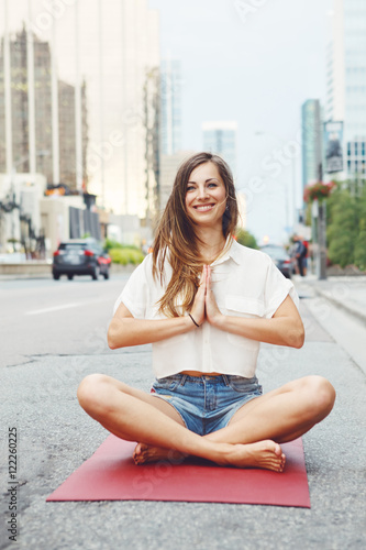 Portrait of slim fit sporty young white Caucasian hippie hipster woman with long blond hair meditating doing yoga exercisers in city street, healthy lifestyle concept.