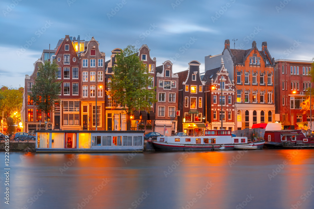 Amsterdam canal Amstel with typical dutch houses and boats during twilight blue hour, Holland, Netherlands.