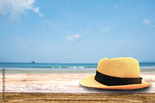 hat on on wood terrace over blue sea and tropical island beach background. Image for Summer Holiday Vacation concept.