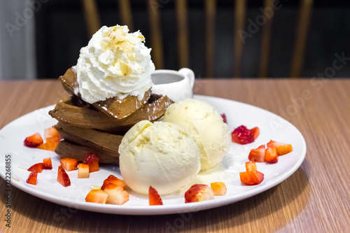Vanilla ice cream with strawberry and black waffle on white plat