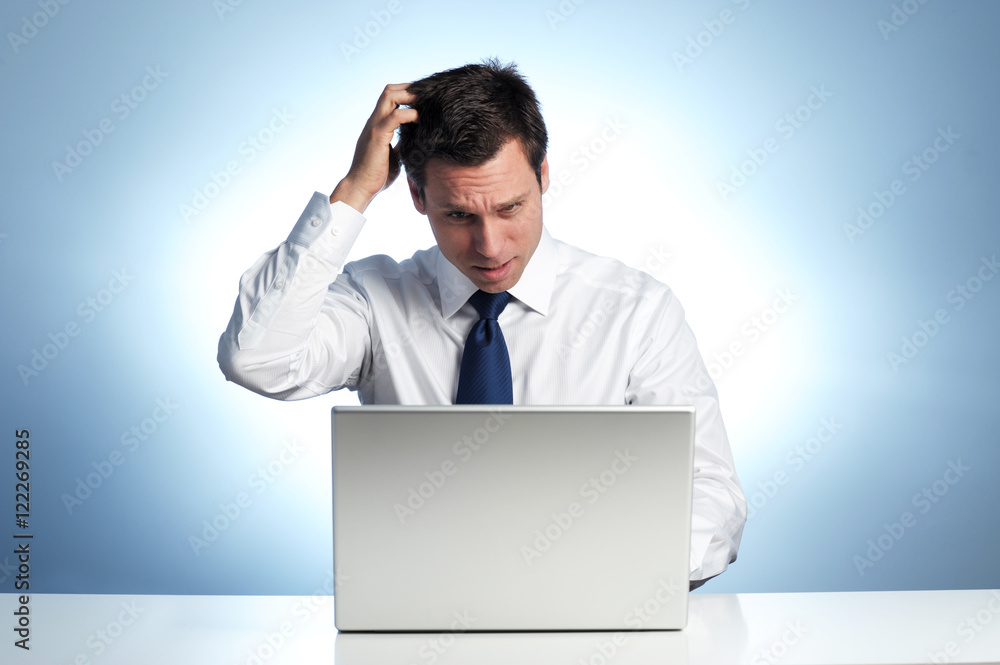 Confused businessman scratching head at laptop computer Confused businessman scratching head at laptop computer